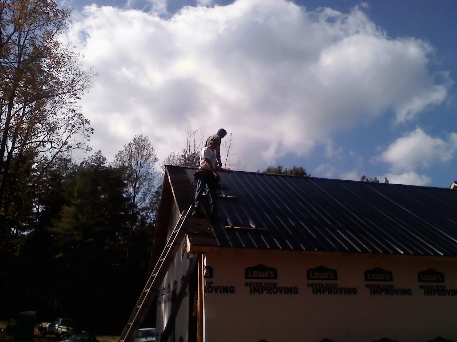 Roofer fastening dark metal panels high against a cloudy sky, from a Roof Inspection job in Greenfield
